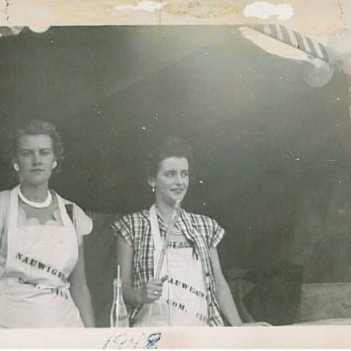 Two volunteers in Nauwigewauk Community Club aprons at a fair booth, 1948